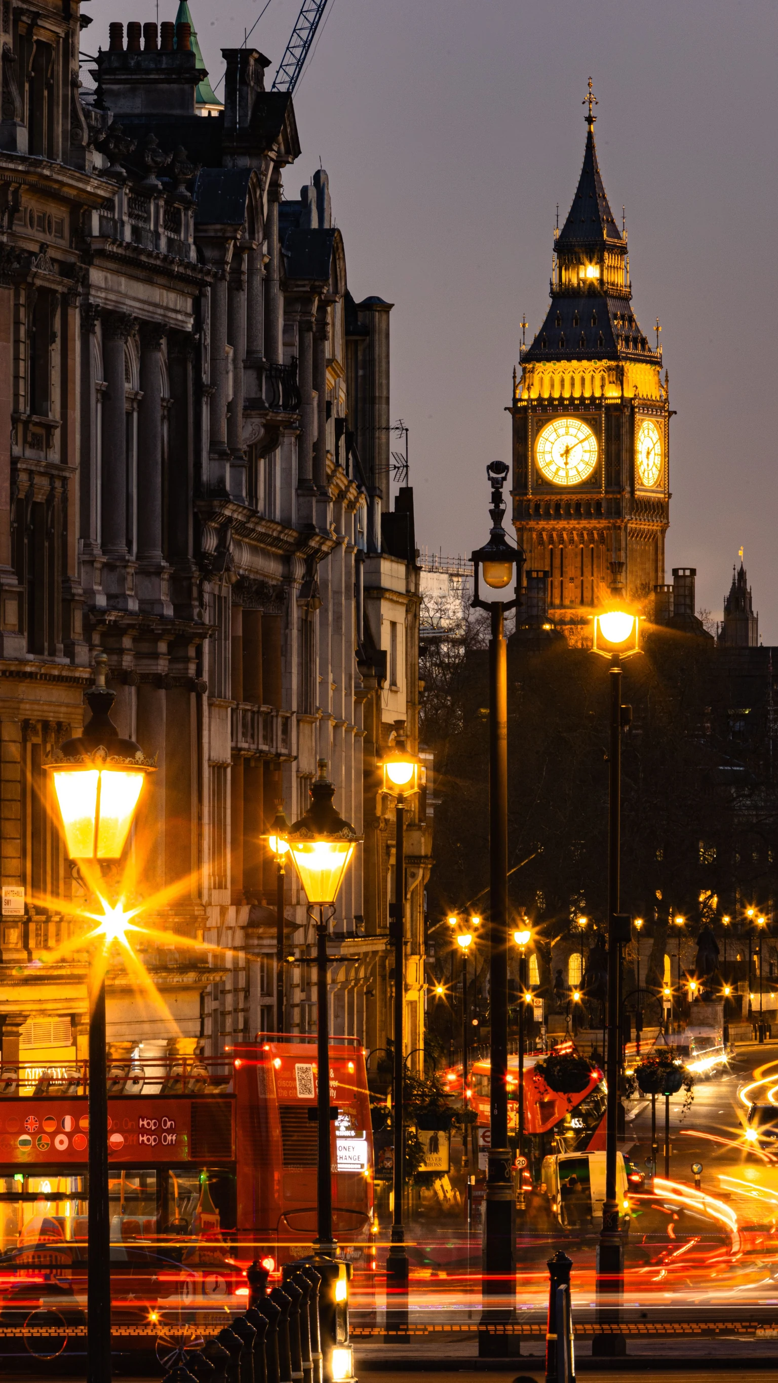 An illuminated clock tower overlooking a busy street with buses at night.